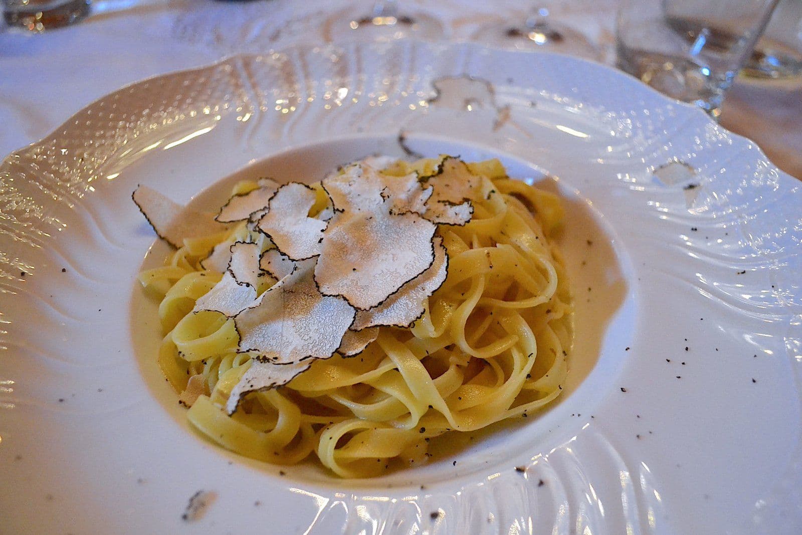 Tagliolini al tartufo: egg pasta topped with shavings of fresh truffle on a white plate
