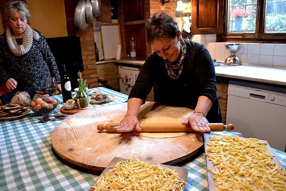 Maria rolling out fresh pasta by hand on a wooden board in the Tuscan farmhouse kitchen