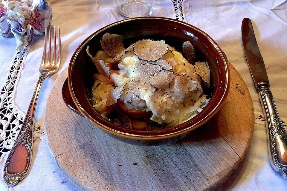 Eggs in a small terracotta dish topped with shavings of fresh truffle