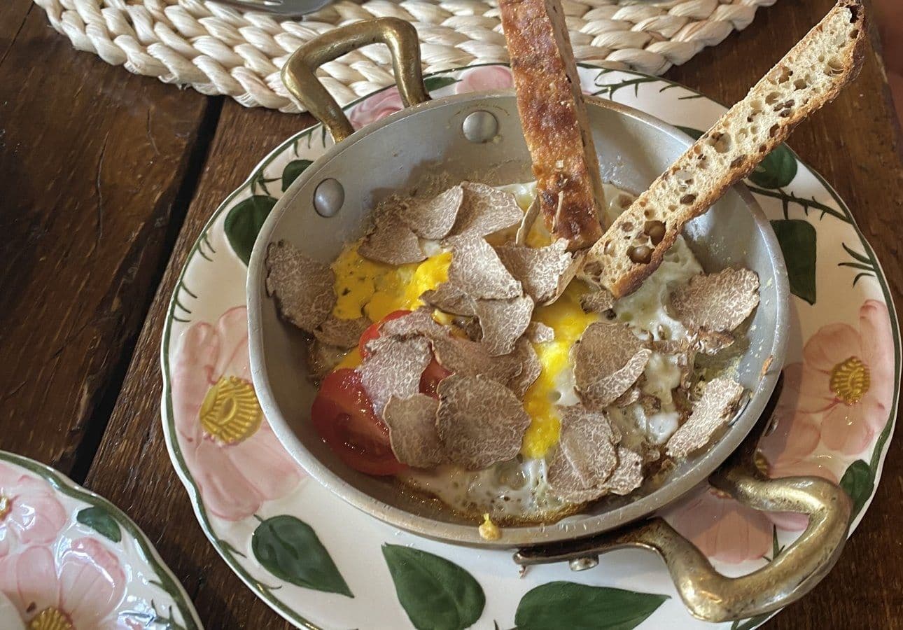 Fried egg with tomato and shavings of fresh truffle in a small pan, served with toasted bread